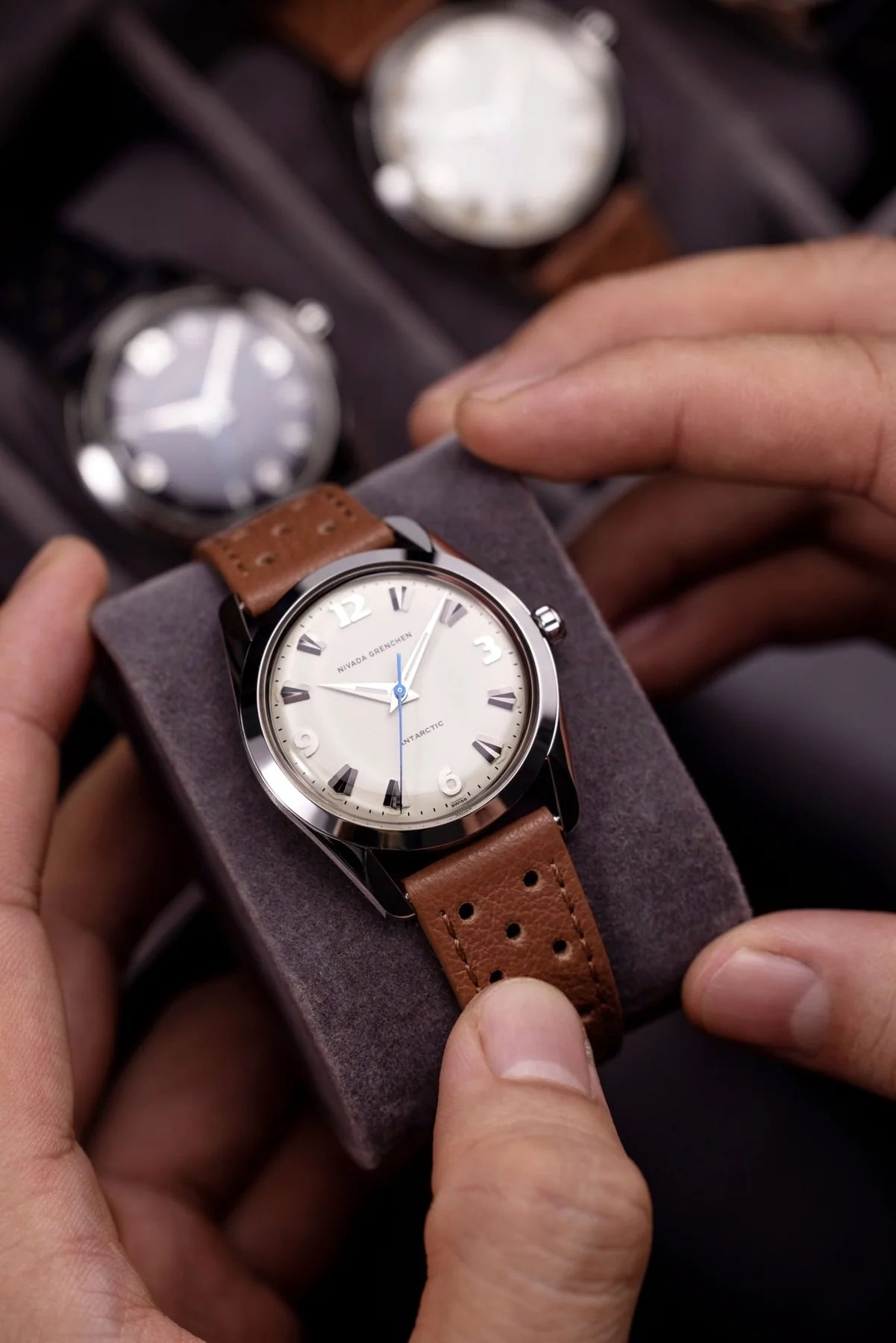 Watch with brown leather strap held by hands on a dark background Nivada Grenchen Antarctic Eggshell Dial White Luminova