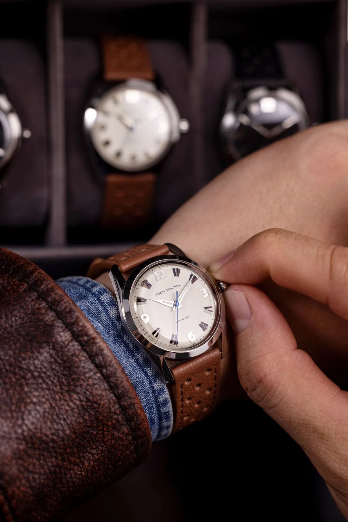 Person adjusting a brown leather watch with a white face and blue  Nivada Grenchen Antarctic Eggshell Dial White Luminovaaccents.